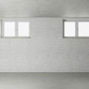An empty, white basement room with two sets of windows at the top of the wall.