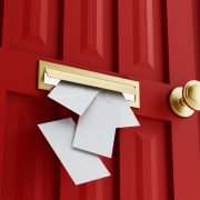 A close up of a red door with a gold colored knob. A mail slot is shown in the center, with several envelopes falling through them.