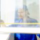 A construction worker in a blue uniform uses a yellow tape measure to measure out a window he is installing.