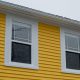 A close up of a yellow home exterior. You can see two double hung windows near the top of the building.