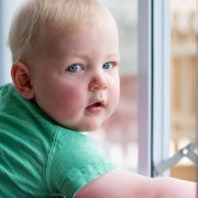 A baby boy looks at the camera as he is perched behind a child proof window.