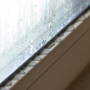 A close up image of the bottom of a window. You can see moisture forming on the window and on the sill holding it, which is a common sign of needing to replace a window.