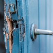 A blue door with chipped and broken wood sticking out of the side.
