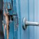 A blue door with chipped and broken wood sticking out of the side.