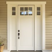 A white entry door with biege tiling surrounding the door. You can see two street lamps and two potted plants on the sides of the door.