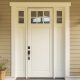 A white entry door with biege tiling surrounding the door. You can see two street lamps and two potted plants on the sides of the door.