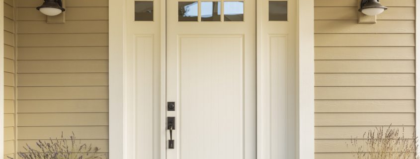 A white entry door with biege tiling surrounding the door. You can see two street lamps and two potted plants on the sides of the door.