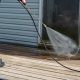 A man in jean shorts uses a power washer to wash grime and mold off of a patio door. You can see the wooden deck he is standing on and the blue finish of the home's exterior.