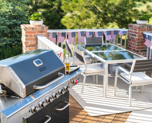 A view of an elevated patio with a dining room set, grill and American flag embordered railways.