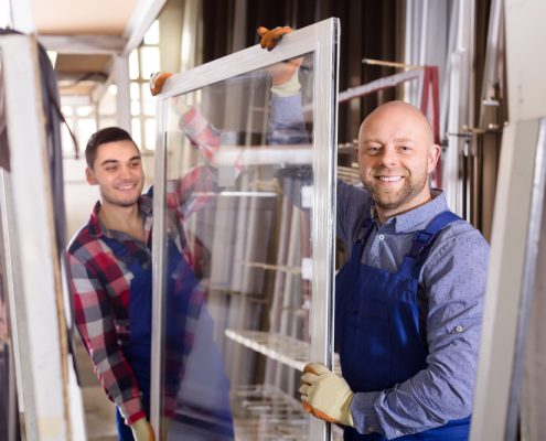 Two workers smile at the camera as they hold opposite ends of a replacement window
