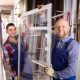 Two workers smile at the camera as they hold opposite ends of a replacement window